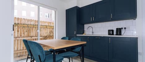 A modern kitchen with dark cabinets, a wooden table, and teal chairs.