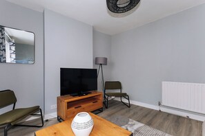 Una sala de estar moderna con un televisor de pantalla plana, un mueble bajo de madera, una lámpara de pie y un radiador.