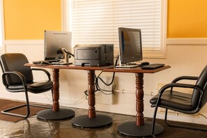 Une pièce comprenant une table en bois, deux chaises de bureau noires, deux écrans Dell, une imprimante et un clavier.