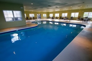 An indoor swimming pool with a curved design, surrounded by lounge chairs and tables.