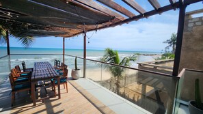 A wooden deck with a table and chairs, overlooking a beach and ocean. - Serenity Residences & Spa - Kokrobite (Kokrobite)