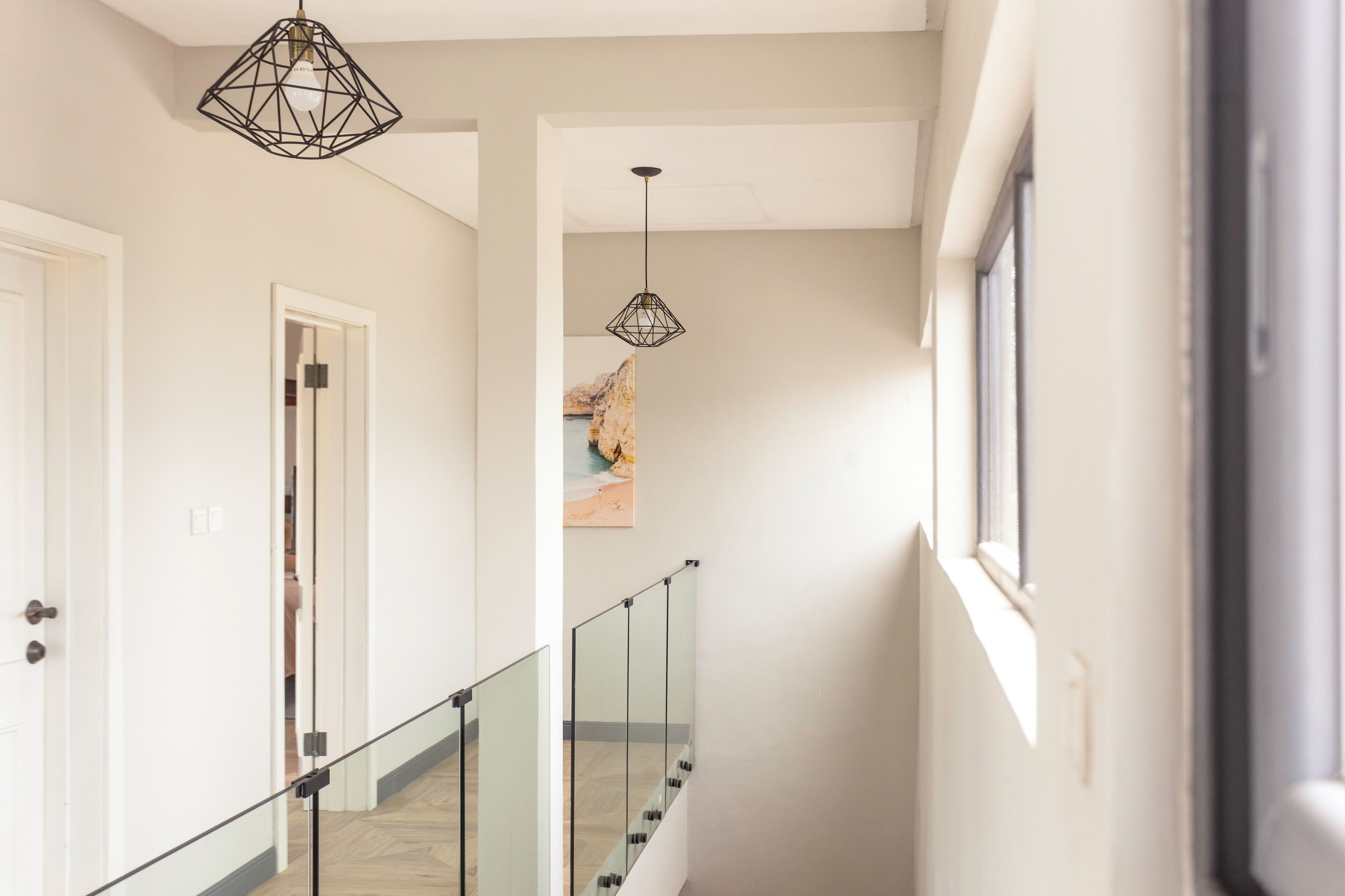 A hallway with a glass railing, a geometric pendant light, and a framed picture on the wall.