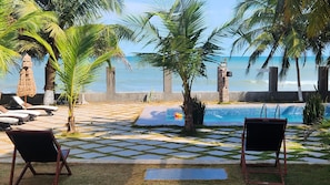 A pool area with lounge chairs, palm trees, and a view of the ocean. - Serenity Residences & Spa - Kokrobite (Kokrobite)