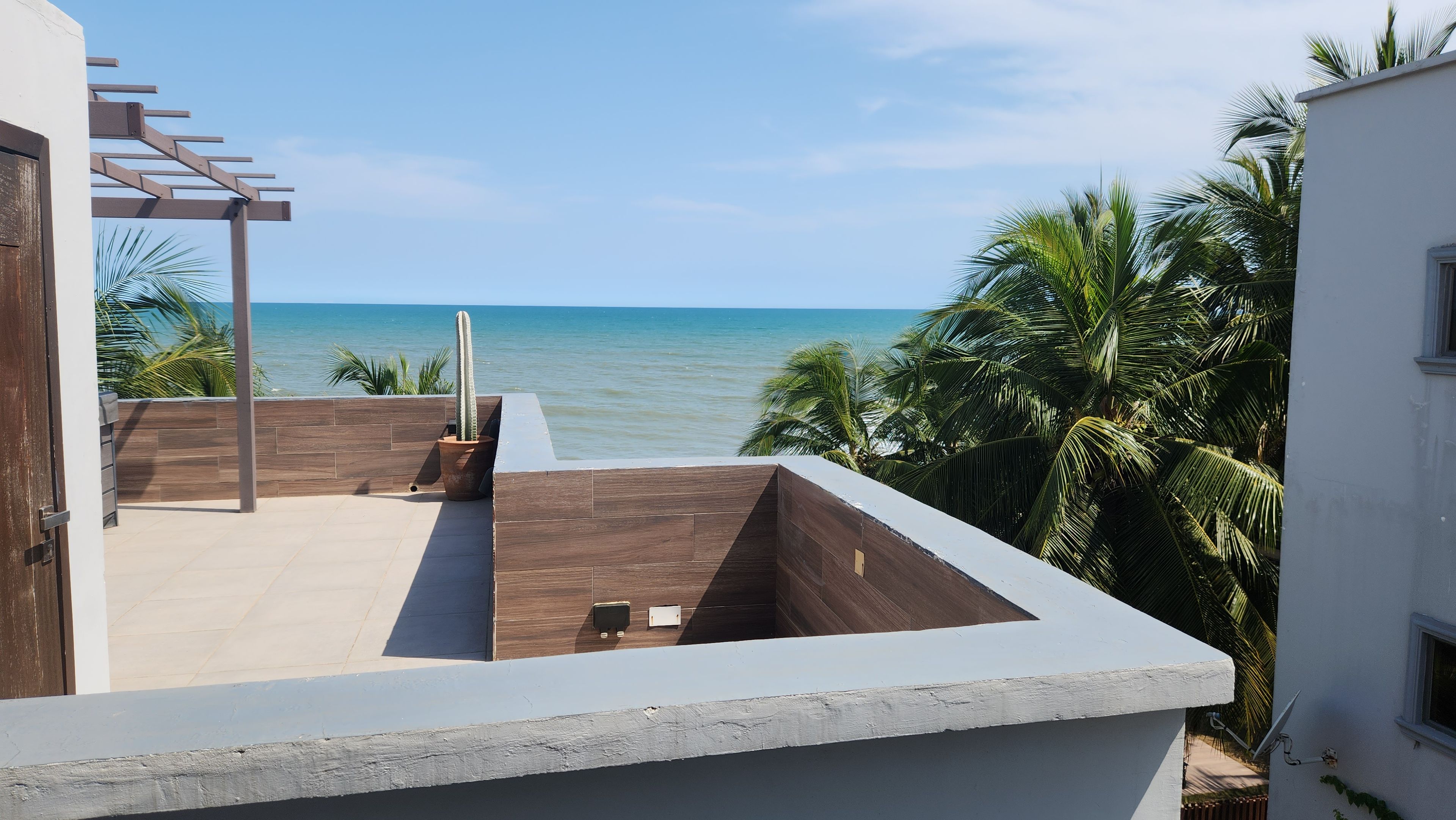 A rooftop terrace with a view of the sea, wooden flooring, and a pergola structure.