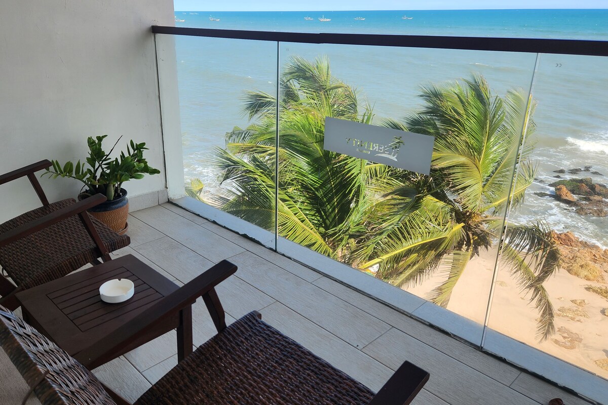 A balcony with a view of the ocean, a potted plant, and a table with a bowl.