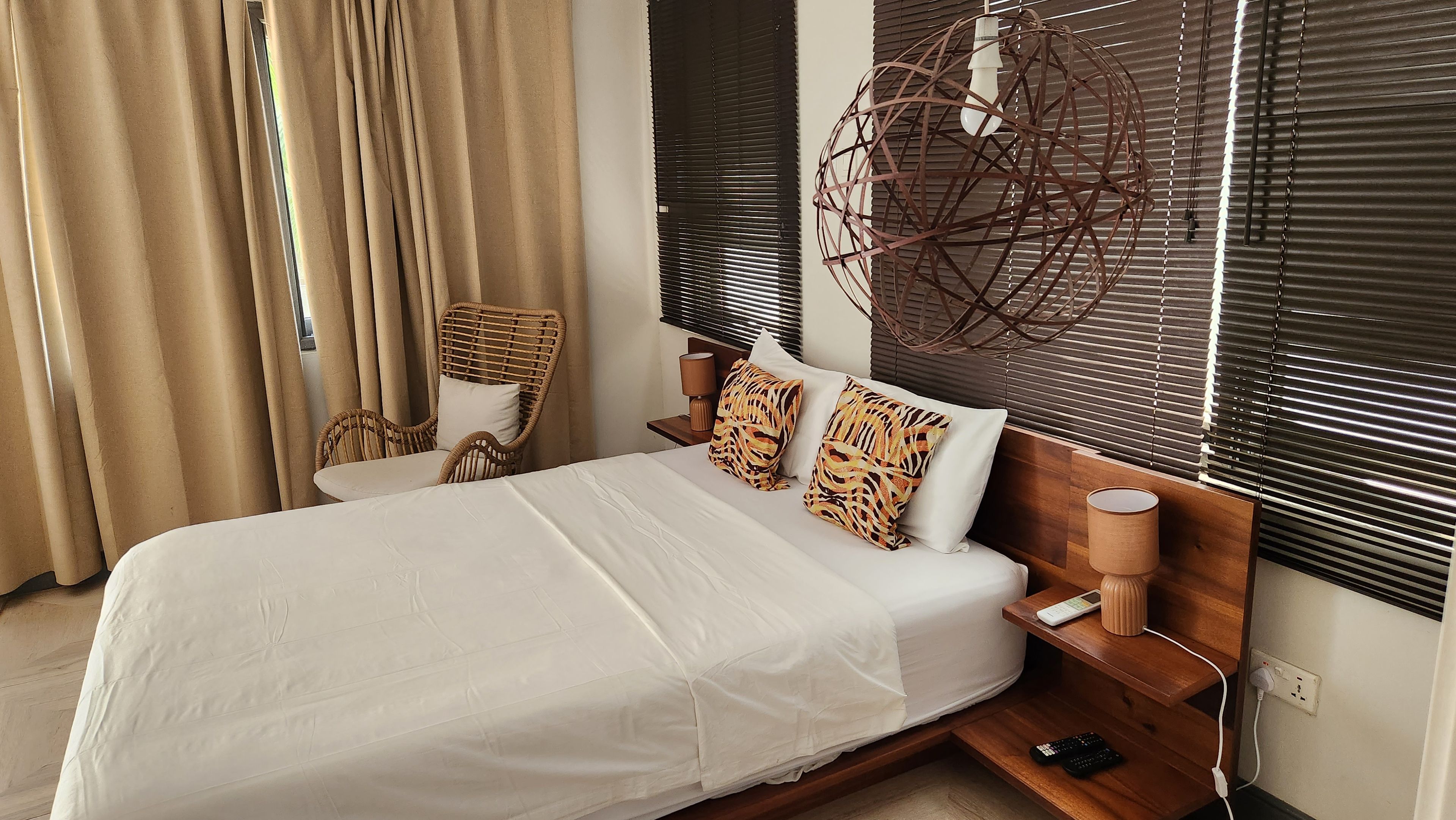 A hotel room with a bed, a chair, a lamp, and a wall-mounted light fixture.