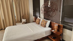 A hotel room with a bed, a chair, a lamp, and a wall-mounted light fixture. - Serenity Residences & Spa - Kokrobite (Kokrobite)