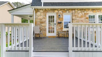 Une maison avec une façade en pierre, un porche à l’avant doté de balustrades blanches et une porte avec un panneau de verre.