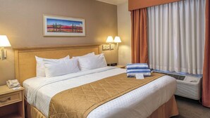 A hotel room with a bed, a nightstand, a lamp, a painting on the wall, and a window with curtains.