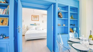A room with a bed, a dining area with a table set for two, and a bookshelf filled with books and decorative items. - L'Horizon - 3 ch climatisé avec vue mer incroyable (Marseille)