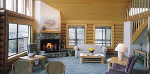 A cozy log cabin interior with a fireplace, a sofa, a coffee table, and a staircase.