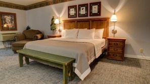 Ein ordentlich eingerichtetes Schlafzimmer mit einem großen Bett, Nachttischen mit Lampen, einer Bank und einem Sessel.