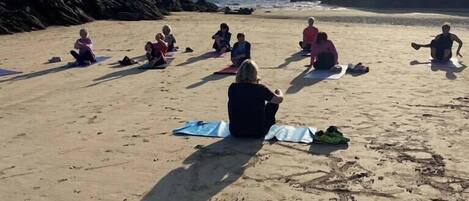 Un grup de persones assegudes sobre esteves a una platja sorrenca, amb roques al fons.