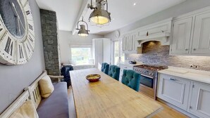 Una cocina moderna con armarios blancos, una pared de acento de piedra, un reloj grande y un comedor con mesa de madera y sillas tapizadas en azul.