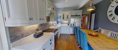 Una cocina moderna con armarios blancos, encimera de madera y comedor con sillas azules.