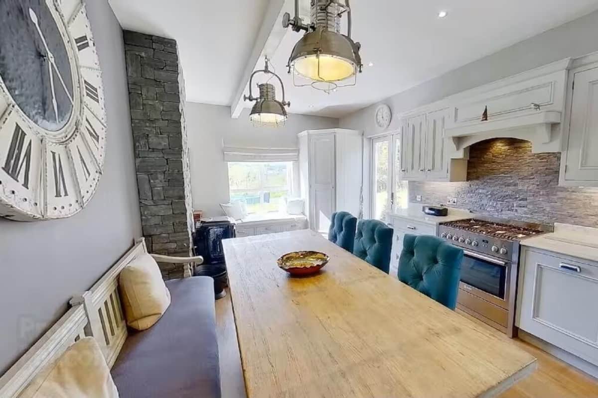 Una cocina moderna con una pared de acento de piedra, un reloj grande y una mesa de comedor de madera.