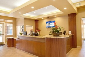 Un espace d’accueil d’hôtel avec un comptoir de réception en bois, un téléviseur à écran plat fixé au mur et une plante en pot posée sur le comptoir.