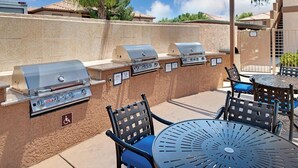 An outdoor grill area with multiple barbecue stations, outdoor seating with chairs and a table, and a covered patio area.