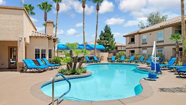 A pool area with lounge chairs, palm trees, and a building with a tiled roof.