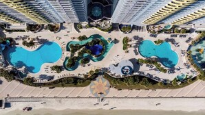 Eine Vogelperspektive zeigt einen luxuriösen Urlaubsort mit mehreren Schwimmbecken, einem Strand und Hochhäusern.