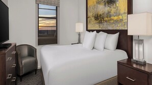 Ein Hotelzimmer mit einem großen Bett, einem Sessel, einem Schreibtisch, einem Fernseher, einem Fenster mit Aussicht und einem Bild an der Wand.