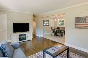 Ein Wohnzimmer mit Flachbildfernseher, grauem Sofa, Couchtisch und Essbereich mit Tisch und Stühlen.