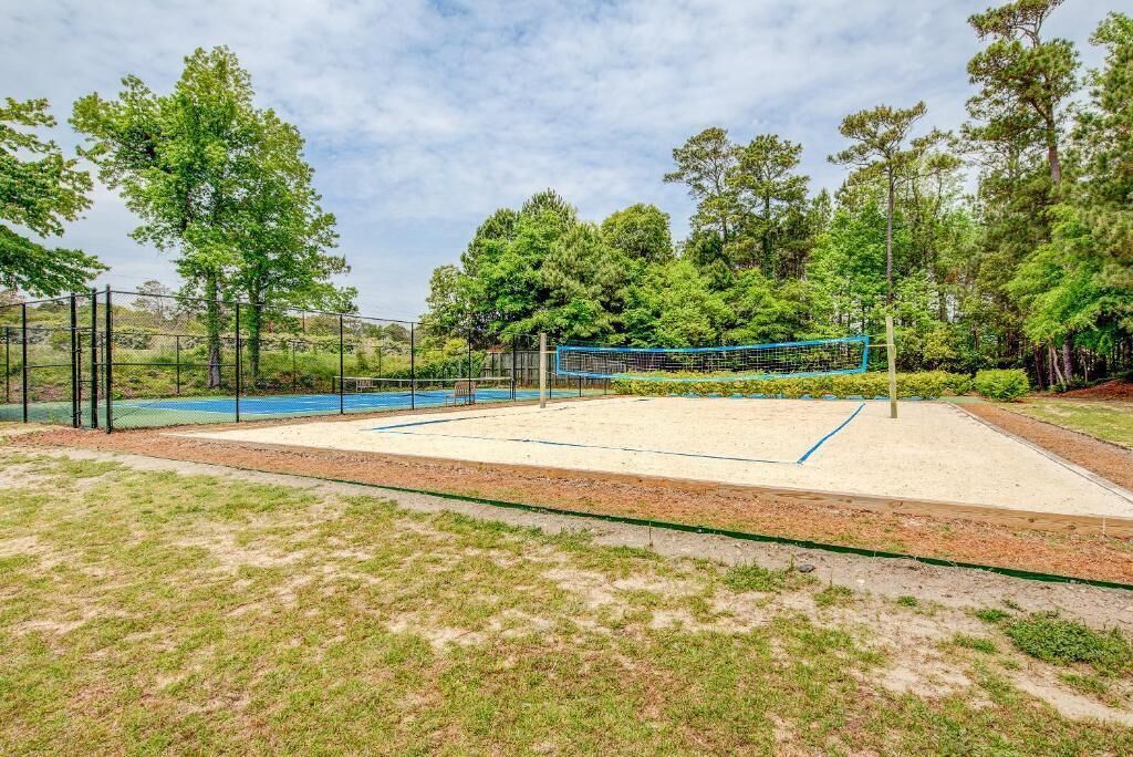 Una cancha de tenis al aire libre con red, rodeada de árboles y una valla.