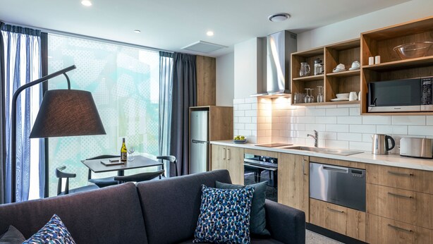 A modern kitchen with wooden cabinets, a built-in microwave, and a dishwasher. - Quest on Cambridge  (Christchurch)