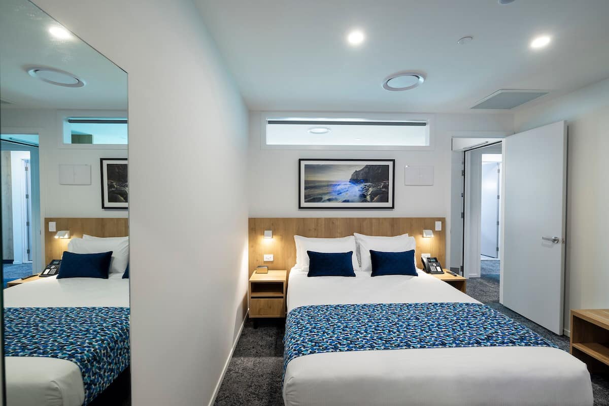 A hotel room with a large bed, bedside tables, a mirror, a picture on the wall, and a door.