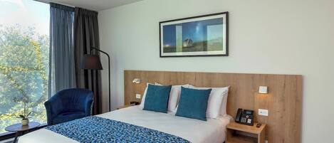 A hotel room with a large bed, a chair, a desk, and a window with curtains.