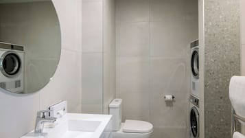 A compact hotel bathroom with a sink, toilet, and two wall-mounted washing machines.