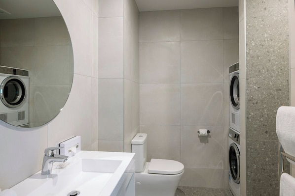 Un baño de hotel pequeño con lavamanos, inodoro y dos lavadoras fijadas a la pared.