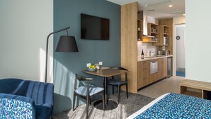 A modern hotel room with a bed, a desk with two chairs, a TV, a lamp, and a kitchenette. - Quest on Cambridge  (Christchurch)