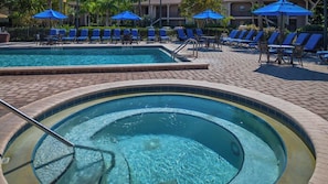 A swimming pool with lounge chairs and umbrellas, surrounded by a brick patio.