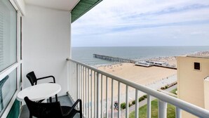A balcony with a view of the beach and pier, a table, and two chairs.