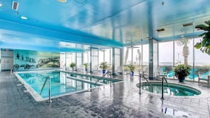 An indoor swimming pool with clear water, tiled floor, and lounge chairs.