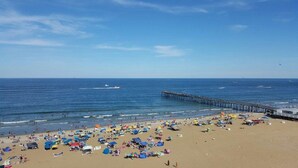 A beach with a pier extending into the ocean, numerous beach umbrellas, and people enjoying the seaside.