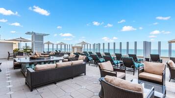 A rooftop terrace with outdoor seating, a fire pit, and a view of the ocean.