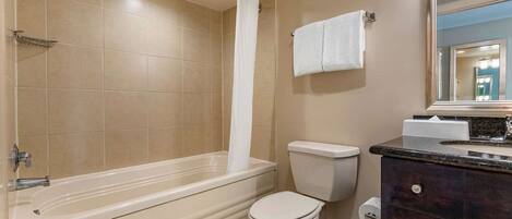 A bathroom with a bathtub, toilet, and vanity with a mirror.