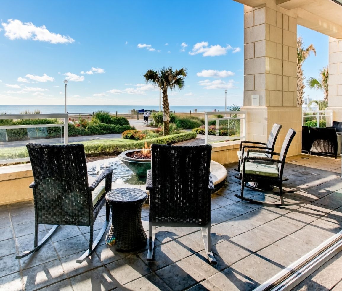 An outdoor patio with wicker chairs, a small fire pit, and a view of the sea.