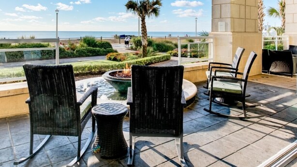 Une terrasse extérieure avec des fauteuils en osier, un petit foyer et une vue sur la mer.