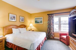A hotel room with a bed, a nightstand, a lamp, a chair, a dresser, a television, and two framed pictures on the wall.