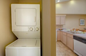 A laundry area with a washing machine and dryer, a kitchen with cabinets and a sink, and a tiled floor.