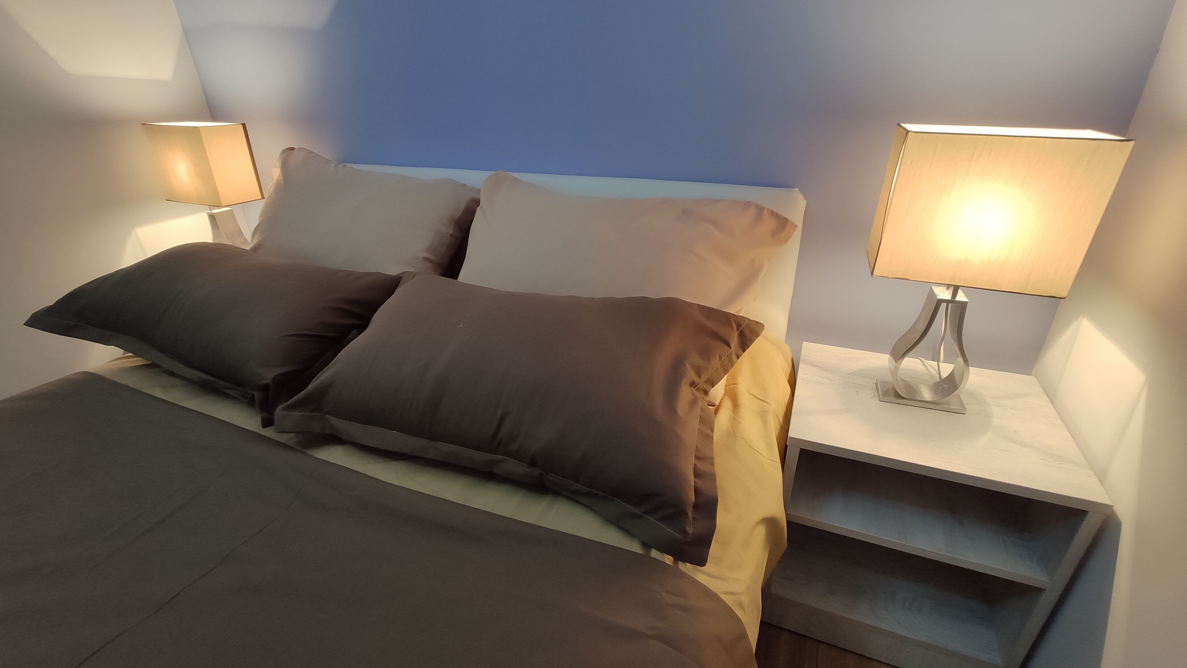 A neatly made bed with a headboard, two bedside lamps, and a nightstand with a drawer.