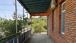 A covered outdoor corridor with a concrete floor, bordered by a metal railing and a brick wall.