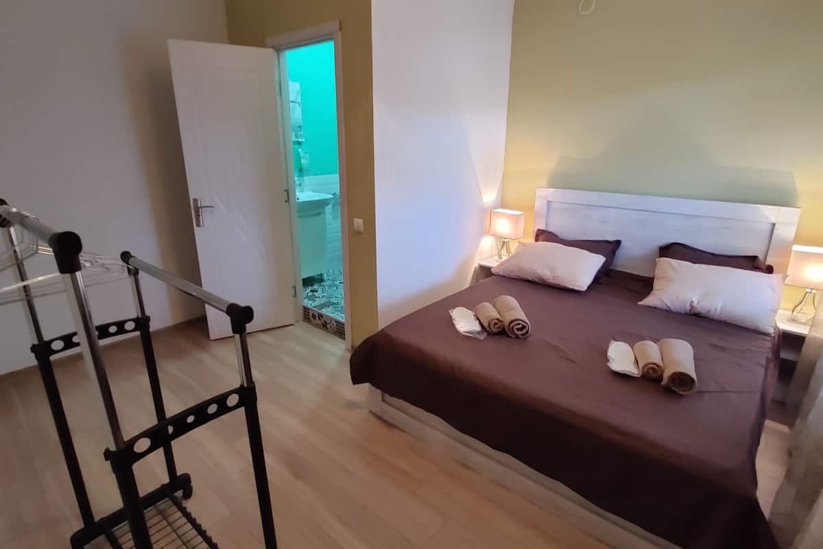 A hotel room with a bed, bedside lamps, and a wheelchair in the corner.