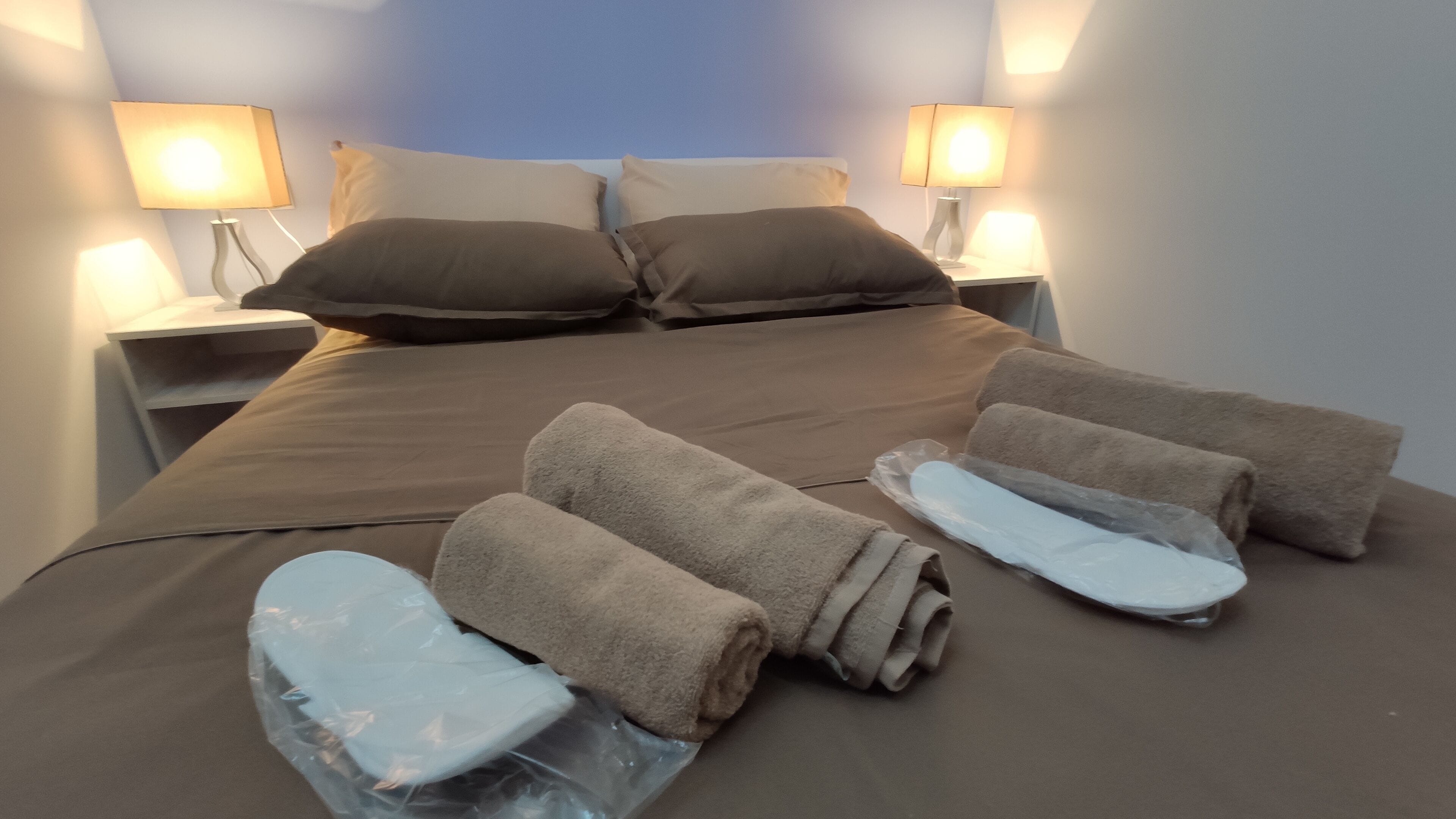 Una cama bien hecha con ropa de cama marrón, dos almohadas y dos toallas enrolladas sobre la cama.