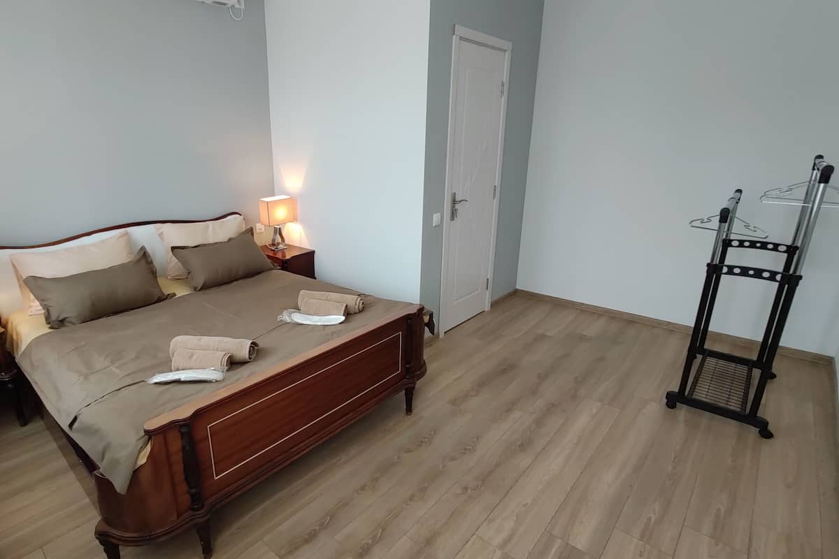A bedroom with a wooden bed, two bedside tables with lamps, a door, and a black metal rack with hangers.