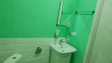 Une salle de bain avec des toilettes blanches, un lavabo blanc et un mur vert.