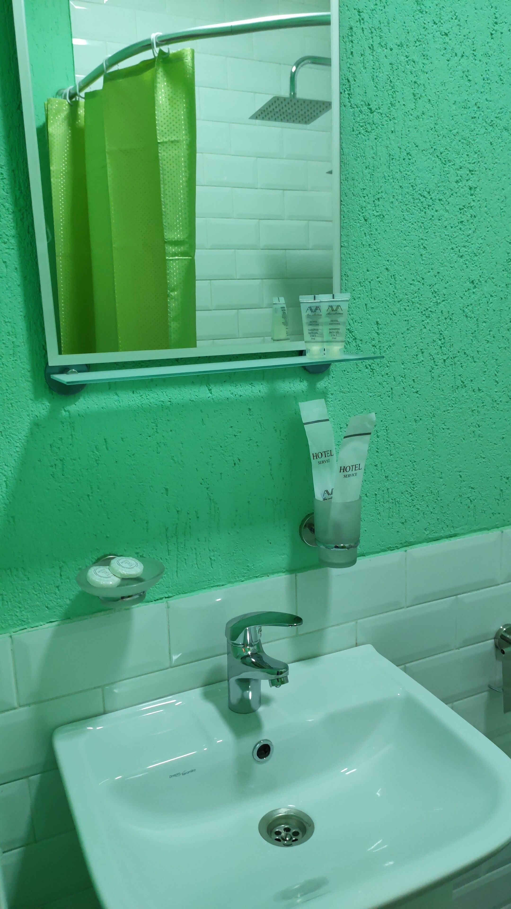 Ein Badezimmer mit grüner Wand, einem weißen Waschbecken, einem Spiegel und Pflegeprodukten auf einem Regal.
